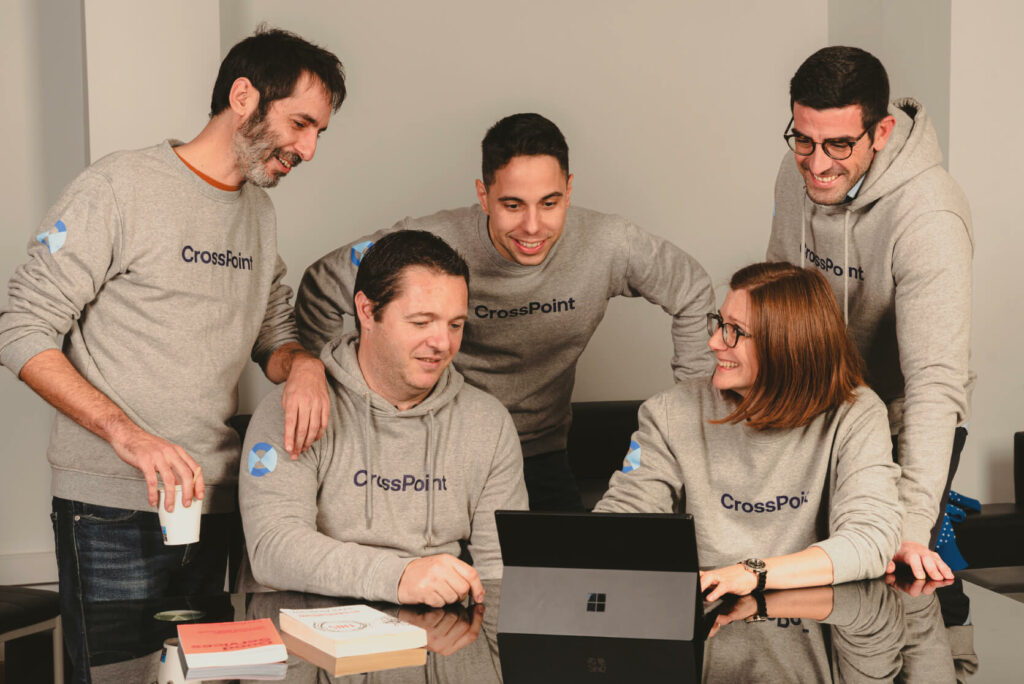 Varios miembros del equipo CossPoint sonr&iacute;en mientras consultan algo en una Suface, alrededor de una mesa